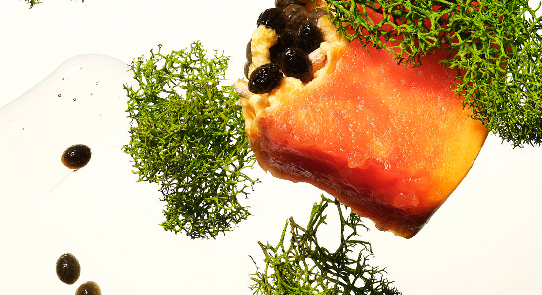 Close-up of a piece of raw fish with green herbs and black seeds on a white background