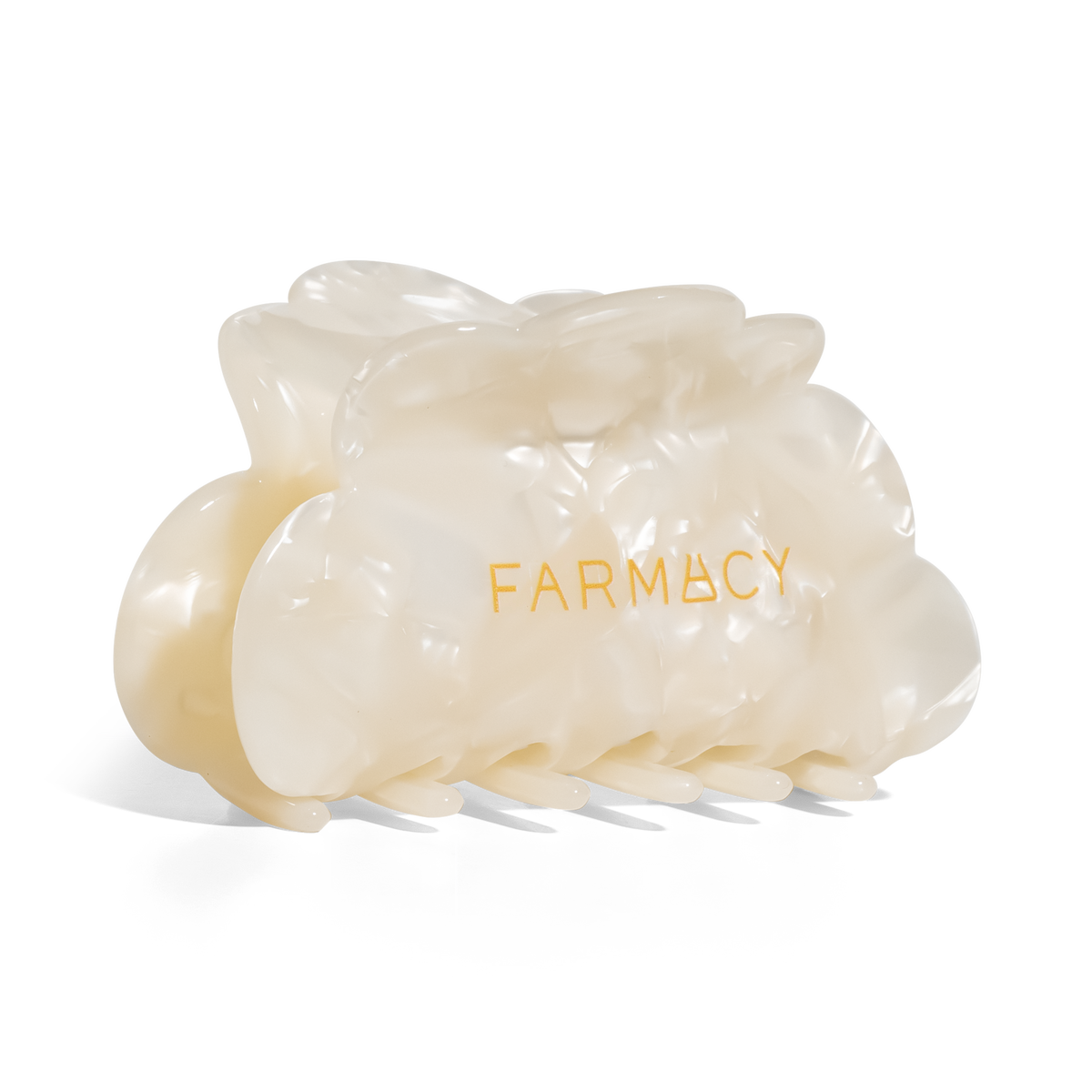 An off-white translucent claw hair clip with the brand name 'FARMACY' printed in gold on the front, set against a plain white background