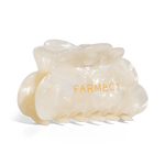 An off-white translucent claw hair clip with the brand name 'FARMACY' printed in gold on the front, set against a plain white background
