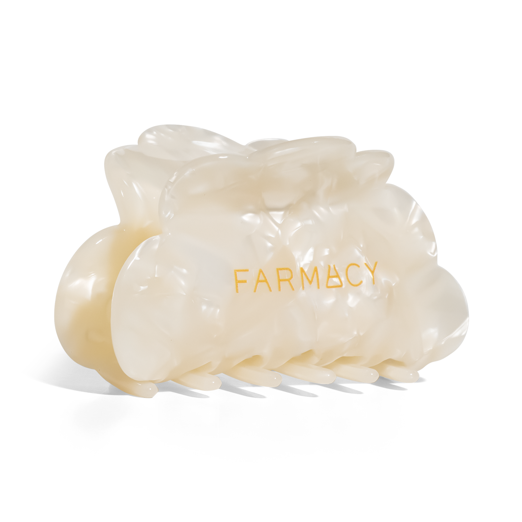 An off-white translucent claw hair clip with the brand name 'FARMACY' printed in gold on the front, set against a plain white background