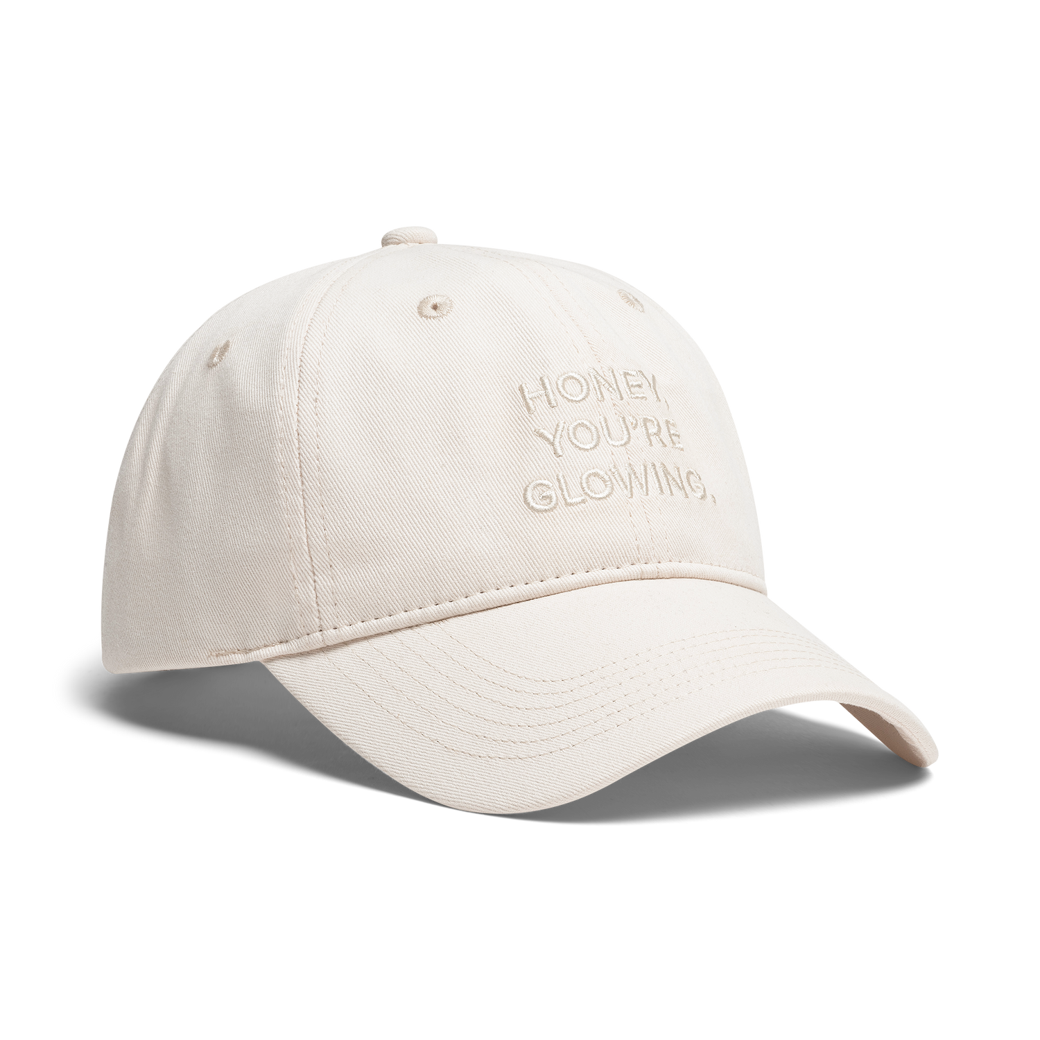 A light beige baseball cap with 'HONEY, YOU'RE GLOWING,' embroidered on the front, shown against a plain white background