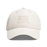 A light beige baseball cap with 'HONEY, YOU'RE GLOWING,' embroidered on the front, shown against a plain white background