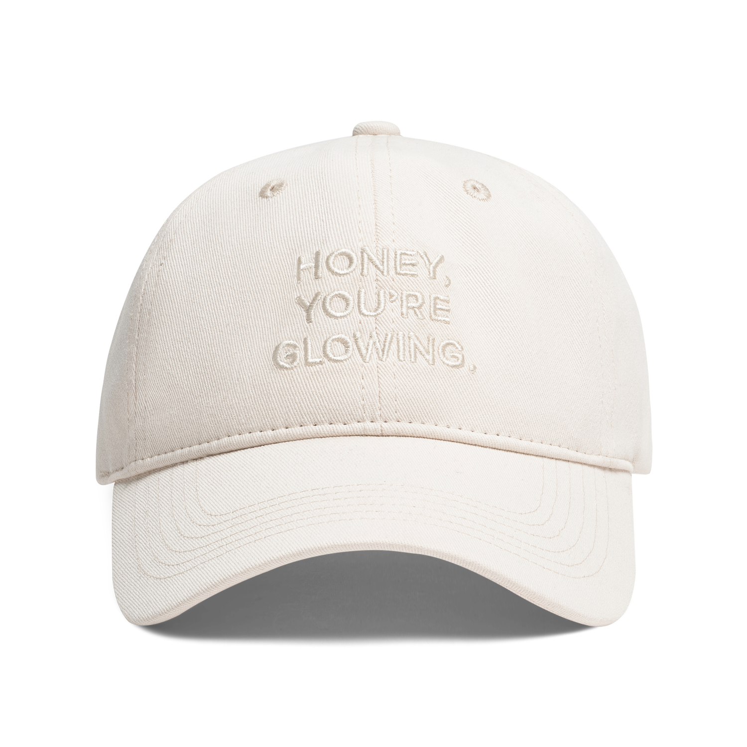A light beige baseball cap with 'HONEY, YOU'RE GLOWING,' embroidered on the front, shown against a plain white background