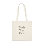 An off-white canvas tote bag with long handles, featuring the text 'Wash Your Face'' with the Farmacy logo on a white background