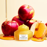 An open bottle of Farmacy Honey Potion Plus Mini sitting in front of apples with honey being poured on them