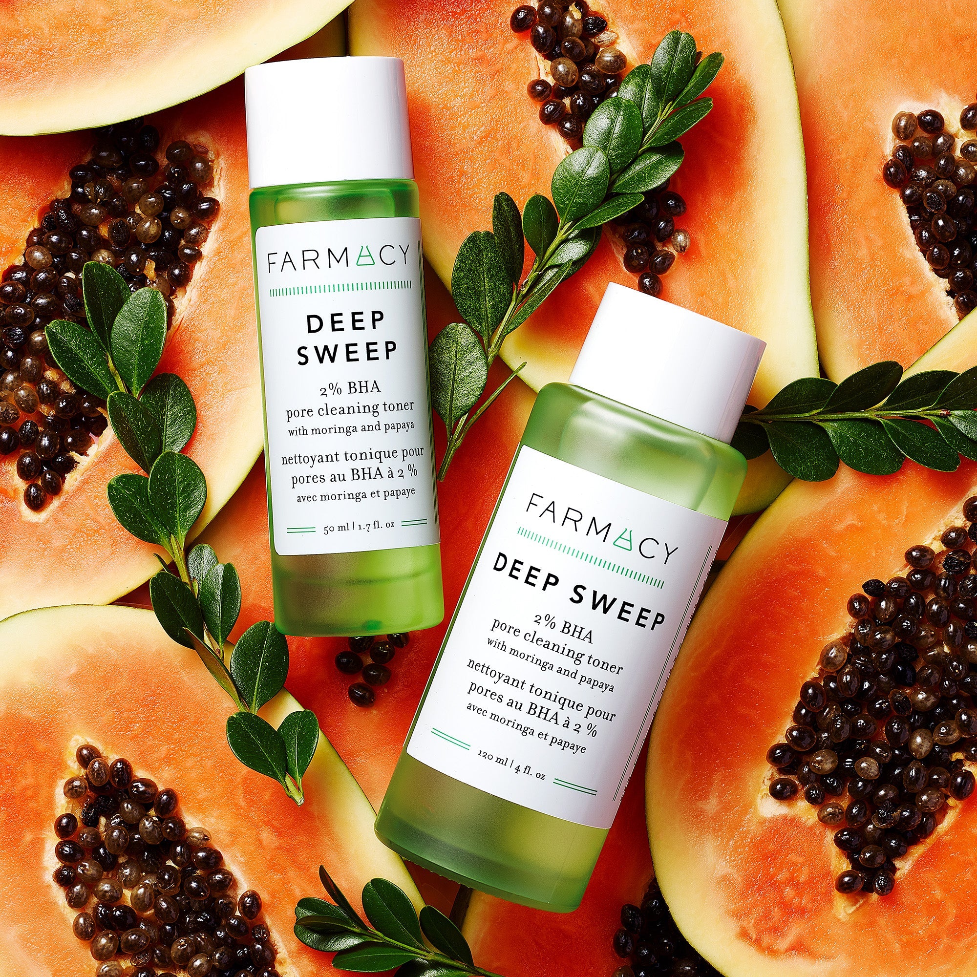Two bottles of Farmacy's Deep Sweep sitting on top of papayas