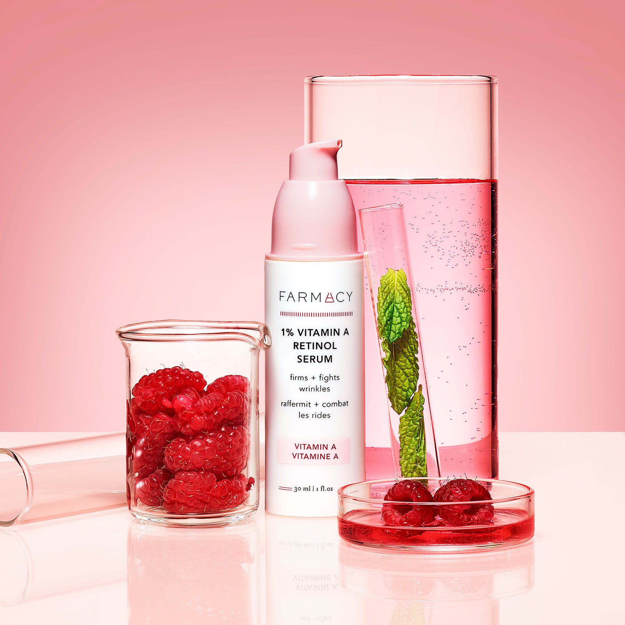 1% Vitamin A Retinol Serum packaging in its cylinder container with the cap off with science beakers behind it filled with pink solution and raspberries, mint in a tube