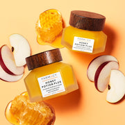 Two bottles of Farmacy Honey Potion Plus lying next to apples and honey