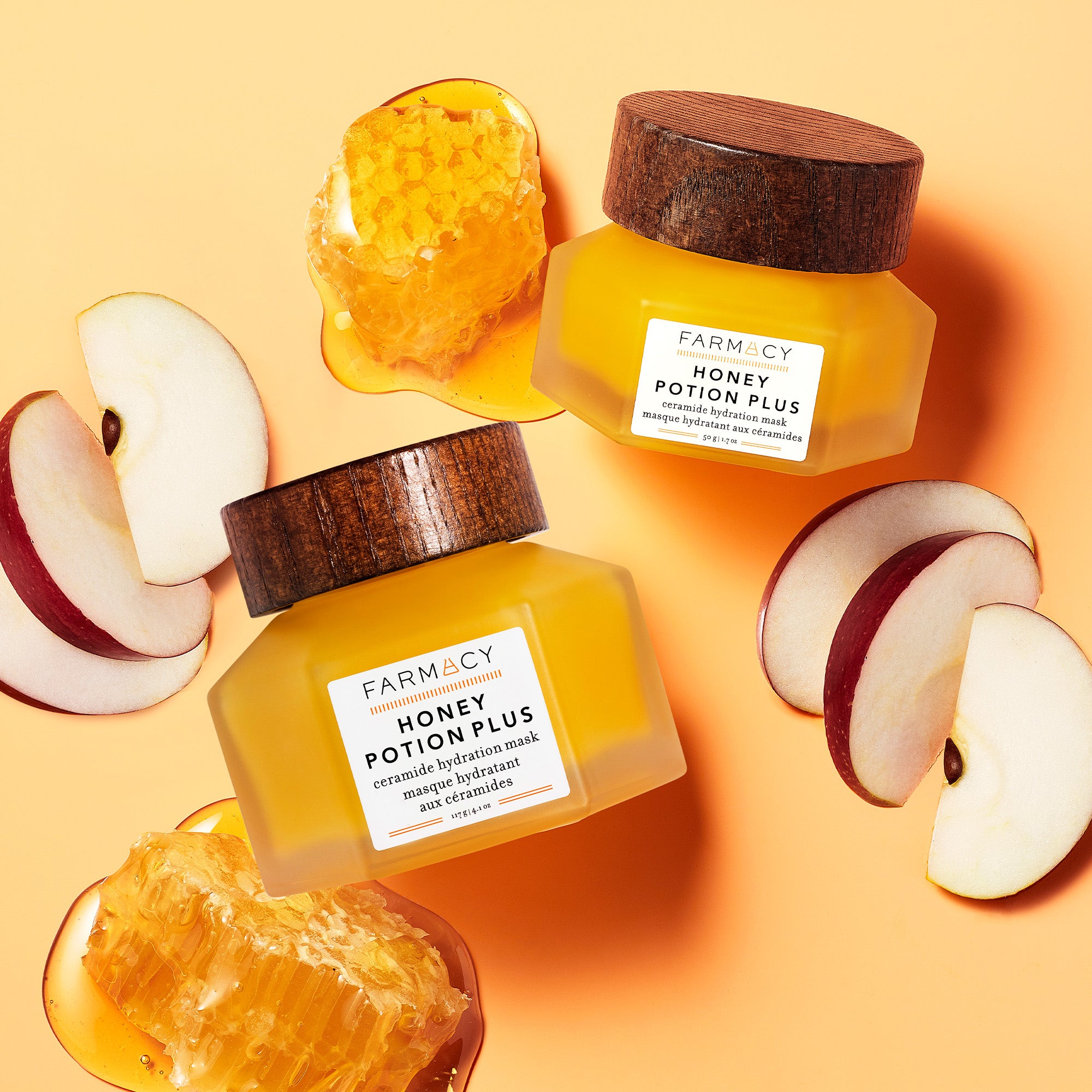 Two bottles of Farmacy Honey Potion Plus lying next to apples and honey