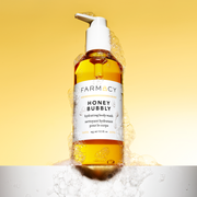 A bottle of Farmacy's Honey Bubbly body wash with soapy bubbles all over the bottle