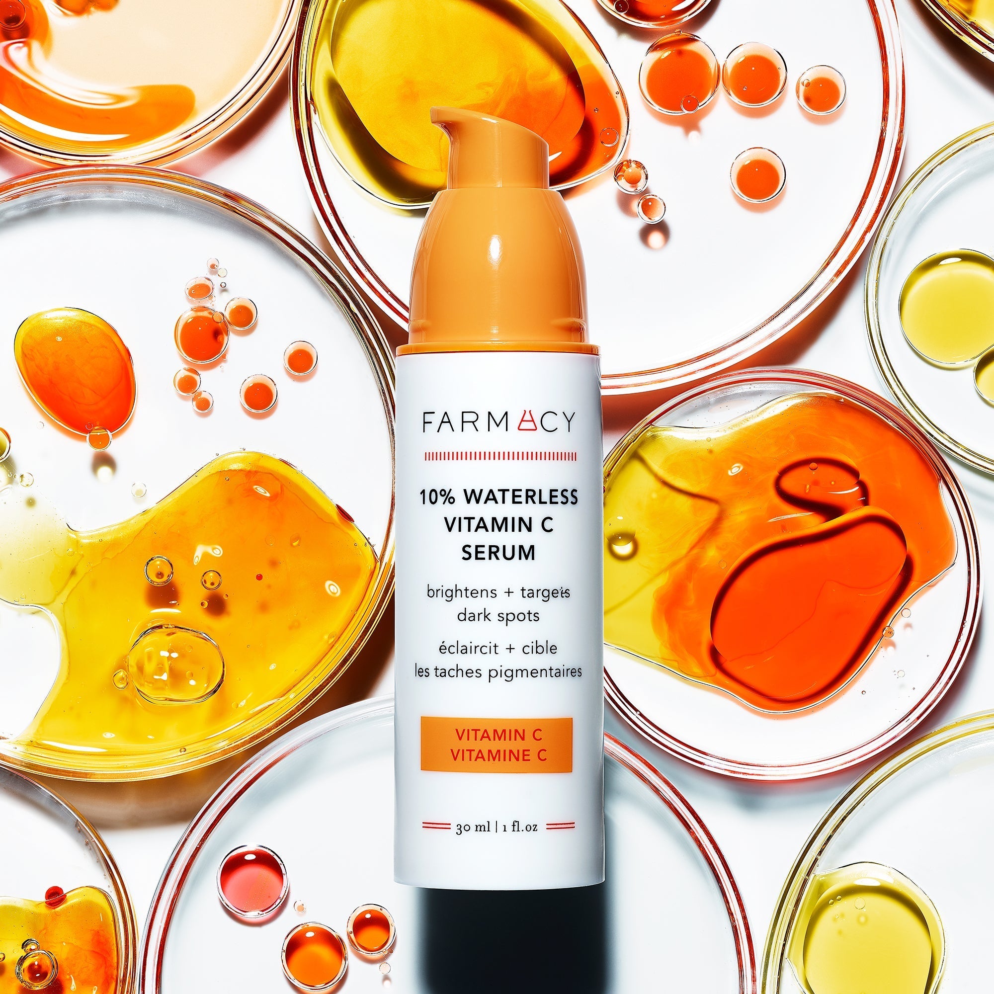 A bottle of 10% Waterless Vitamin C Serum with Vitamin C petri dishes behind it 
