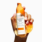 A woman's hand holding a bottle of the 10% Waterless Vitamin C Serum and orange peels